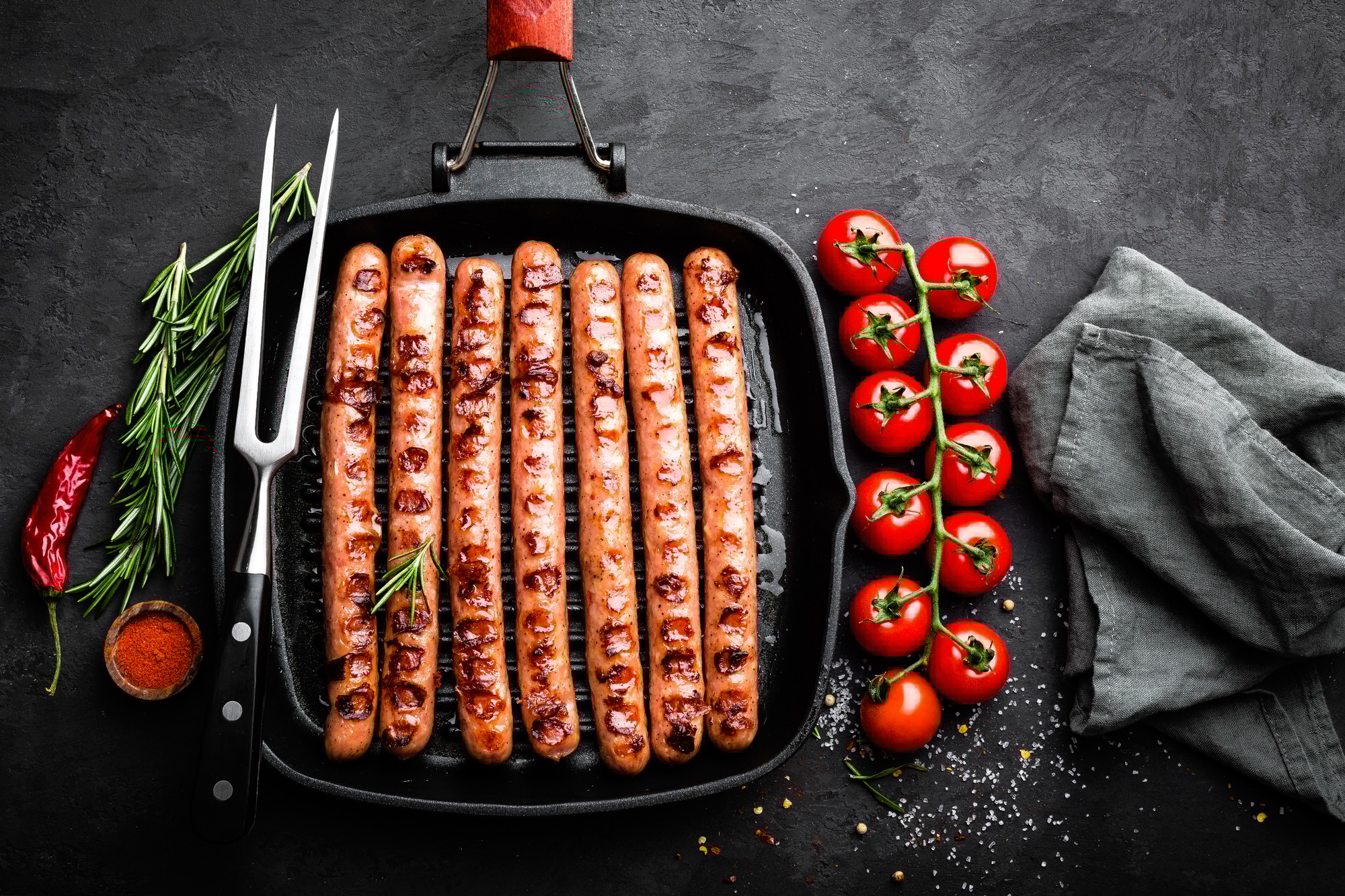 Grilled sausages bratwurst in grill frying-pan on black background. Top view